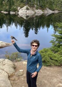 Barb by a mountain lake with a whiskey jack perched on her hand